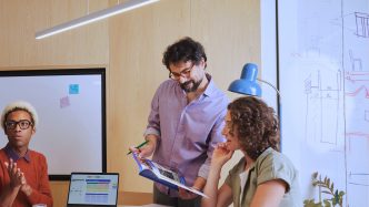 Equipo de tres profesionales revisando material junto a un pizarrón en una oficina